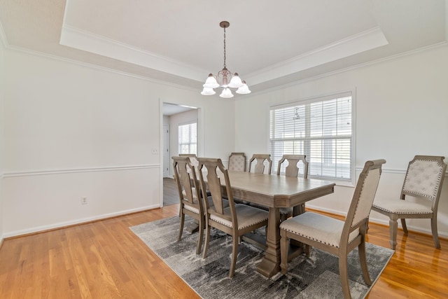 dining space with a raised ceiling, hardwood / wood-style flooring, crown molding, and a notable chandelier