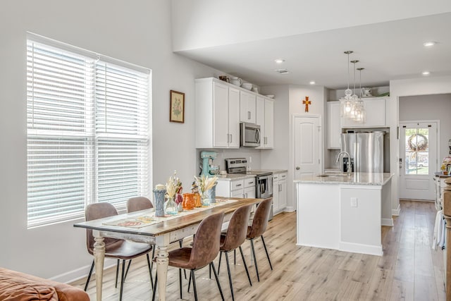 kitchen featuring white cabinetry, hanging light fixtures, light stone counters, a center island with sink, and appliances with stainless steel finishes