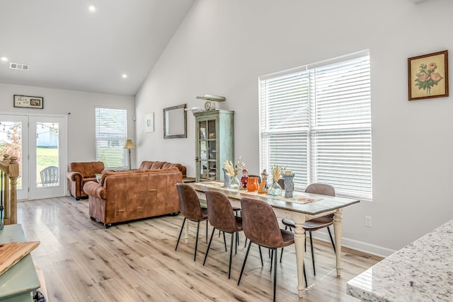 dining area with high vaulted ceiling and light hardwood / wood-style floors