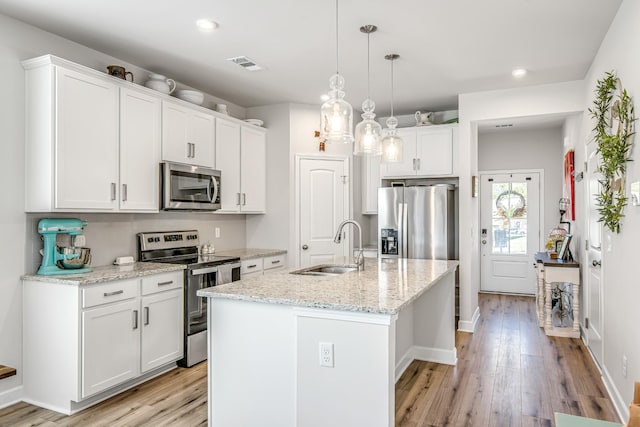 kitchen featuring appliances with stainless steel finishes, light stone counters, sink, white cabinets, and an island with sink