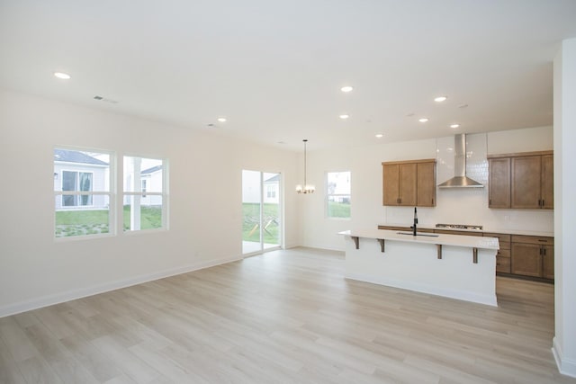 kitchen featuring a breakfast bar, gas stovetop, wall chimney range hood, light hardwood / wood-style floors, and an island with sink