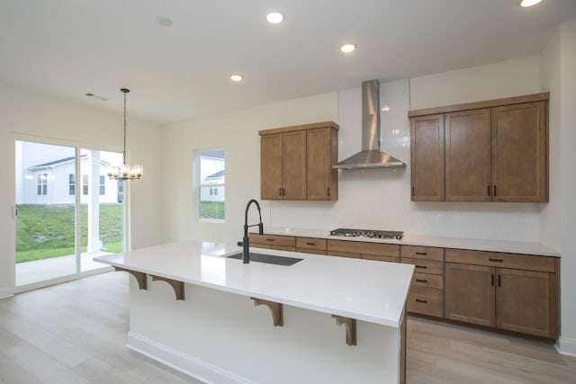 kitchen with a center island with sink, sink, hanging light fixtures, wall chimney exhaust hood, and a kitchen bar