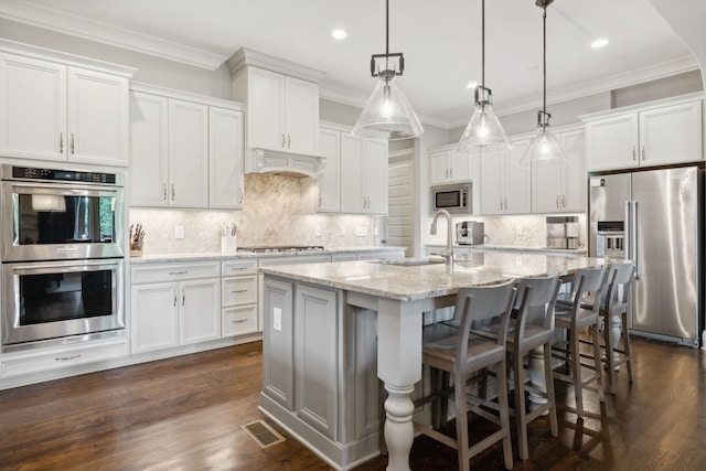 kitchen with appliances with stainless steel finishes, sink, a center island with sink, decorative light fixtures, and white cabinetry