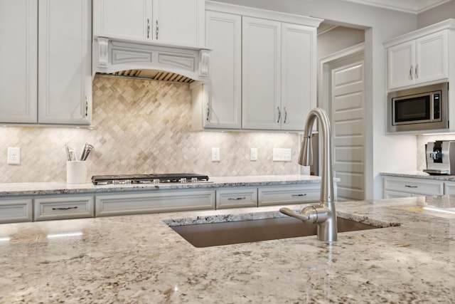 kitchen with light stone countertops, white cabinets, custom range hood, and appliances with stainless steel finishes