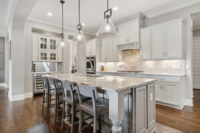 kitchen with custom range hood, white cabinetry, hanging light fixtures, and an island with sink