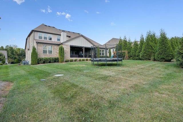 rear view of house with a lawn, a trampoline, and central AC