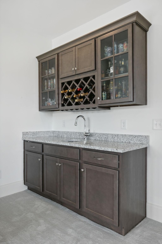 bar featuring dark brown cabinetry, light colored carpet, light stone counters, and sink