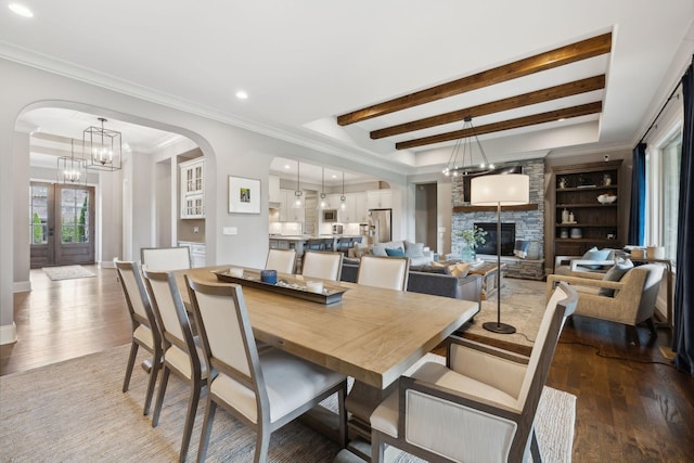 dining area featuring an inviting chandelier, hardwood / wood-style flooring, a stone fireplace, and crown molding