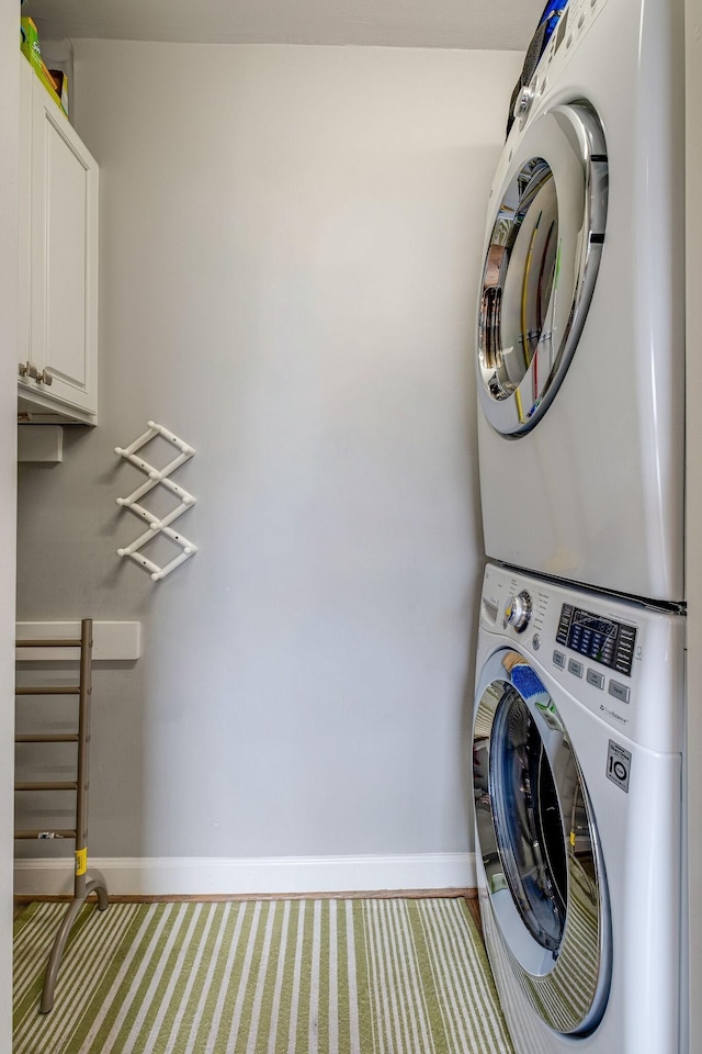 clothes washing area with cabinets and stacked washer / dryer