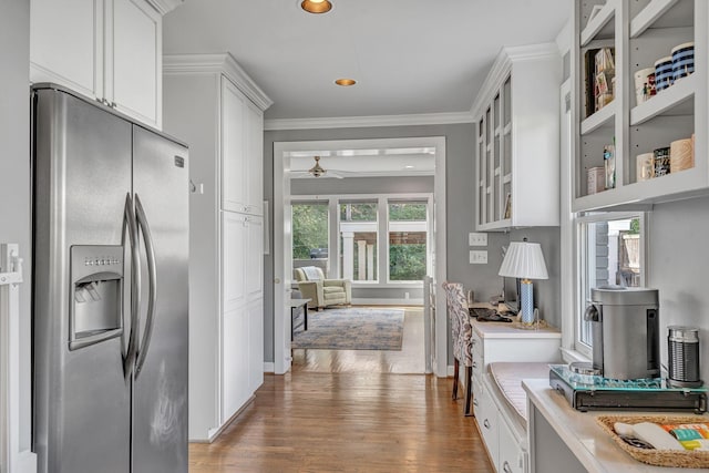 kitchen featuring stainless steel fridge, ornamental molding, ceiling fan, wood-type flooring, and white cabinets