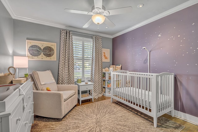 bedroom featuring a crib, wood-type flooring, ceiling fan, and ornamental molding