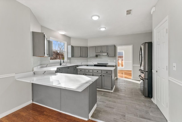 kitchen featuring stainless steel refrigerator, kitchen peninsula, sink, and gray cabinets