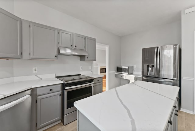 kitchen with appliances with stainless steel finishes, a center island, gray cabinets, and light hardwood / wood-style flooring