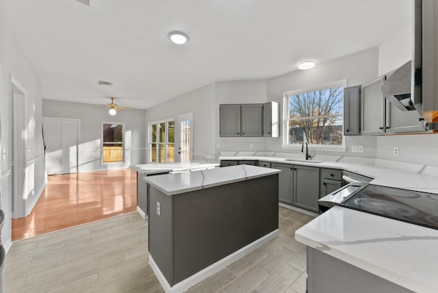 kitchen with a center island, sink, wall chimney exhaust hood, gray cabinets, and ceiling fan