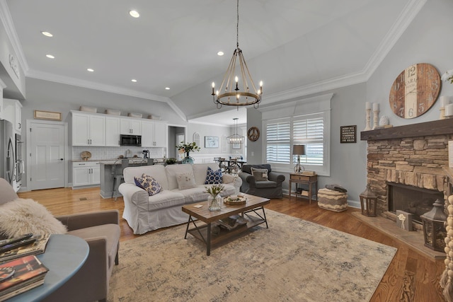 living room with light wood-type flooring, ornamental molding, vaulted ceiling, a notable chandelier, and a stone fireplace