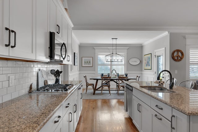 kitchen with stainless steel appliances, a kitchen island with sink, crown molding, sink, and white cabinetry