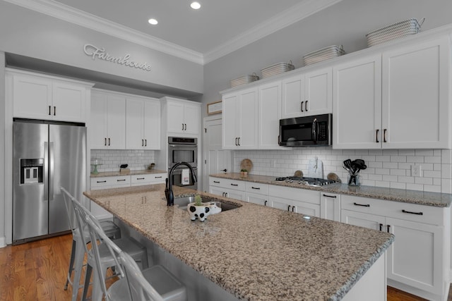 kitchen with appliances with stainless steel finishes, backsplash, white cabinetry, and a kitchen island with sink