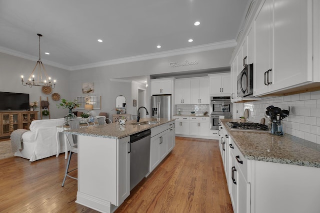 kitchen featuring backsplash, a kitchen island with sink, sink, appliances with stainless steel finishes, and white cabinetry