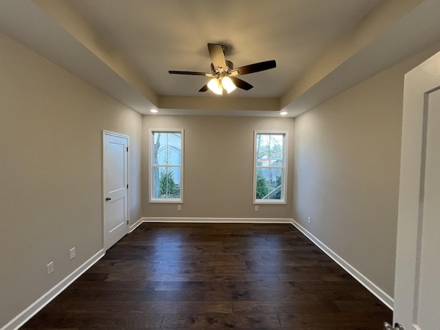 unfurnished room with dark hardwood / wood-style flooring, a tray ceiling, and ceiling fan