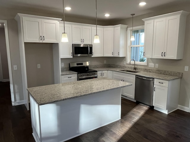 kitchen with stainless steel appliances, sink, white cabinets, a center island, and hanging light fixtures