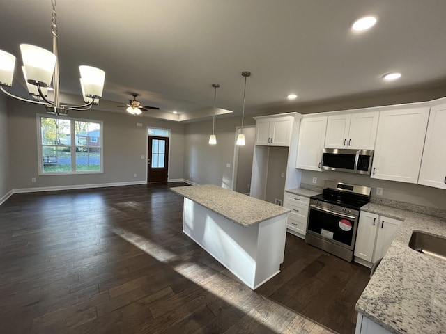 kitchen with appliances with stainless steel finishes, ceiling fan with notable chandelier, white cabinetry, and hanging light fixtures