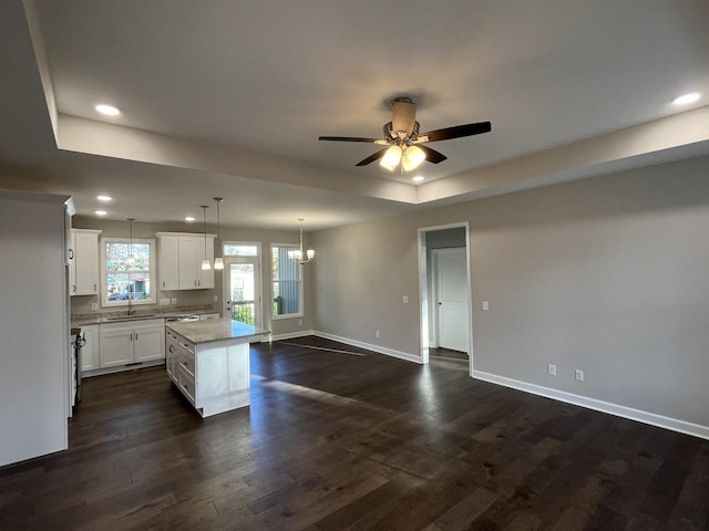 kitchen with dark wood-type flooring, hanging light fixtures, a kitchen island, white cabinets, and ceiling fan with notable chandelier