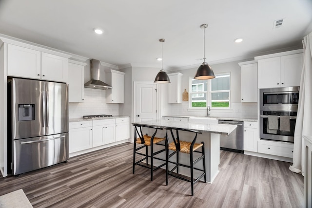 kitchen featuring stainless steel appliances, wall chimney range hood, pendant lighting, white cabinets, and a center island