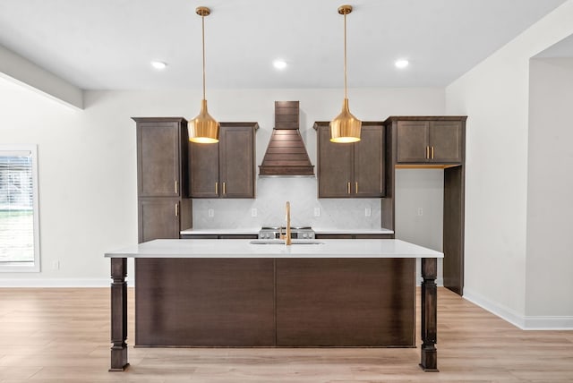 kitchen featuring decorative backsplash, an island with sink, decorative light fixtures, and custom exhaust hood