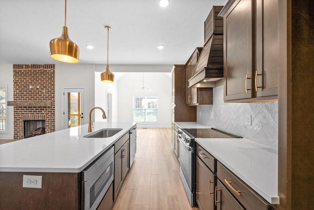 kitchen with decorative backsplash, stainless steel appliances, a kitchen island with sink, sink, and decorative light fixtures