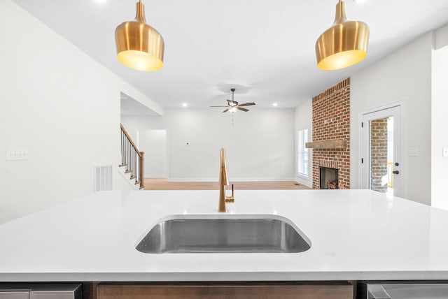 kitchen featuring a fireplace, ceiling fan, sink, and hanging light fixtures