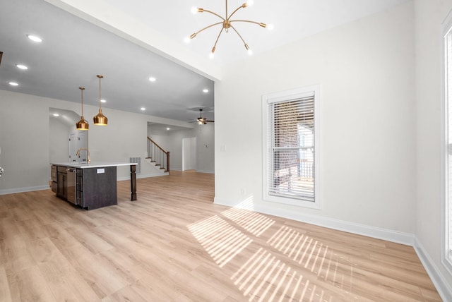 kitchen featuring ceiling fan with notable chandelier, a kitchen island with sink, sink, light hardwood / wood-style flooring, and hanging light fixtures