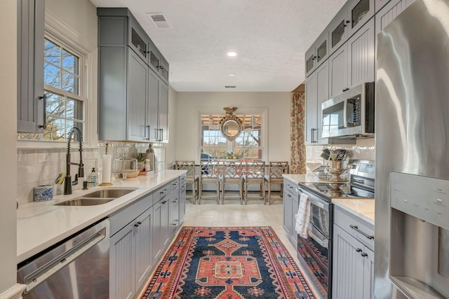 kitchen with sink, a textured ceiling, appliances with stainless steel finishes, gray cabinets, and backsplash