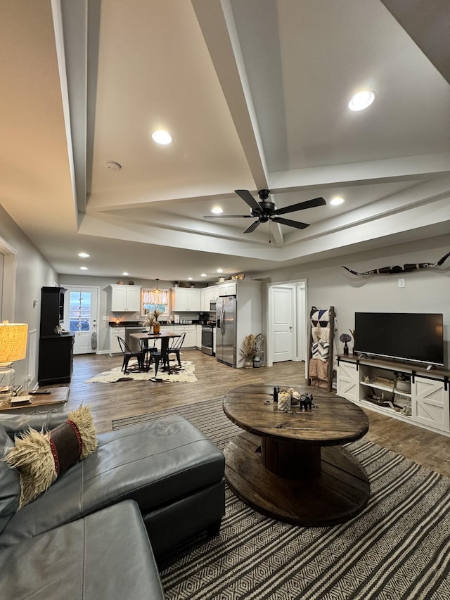 living room with wood-type flooring, a raised ceiling, and ceiling fan