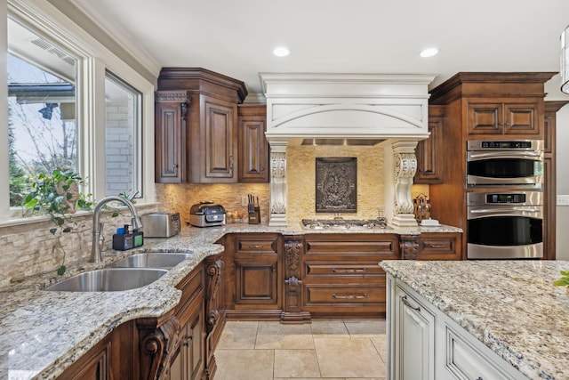 kitchen with sink, stainless steel appliances, light stone counters, premium range hood, and backsplash