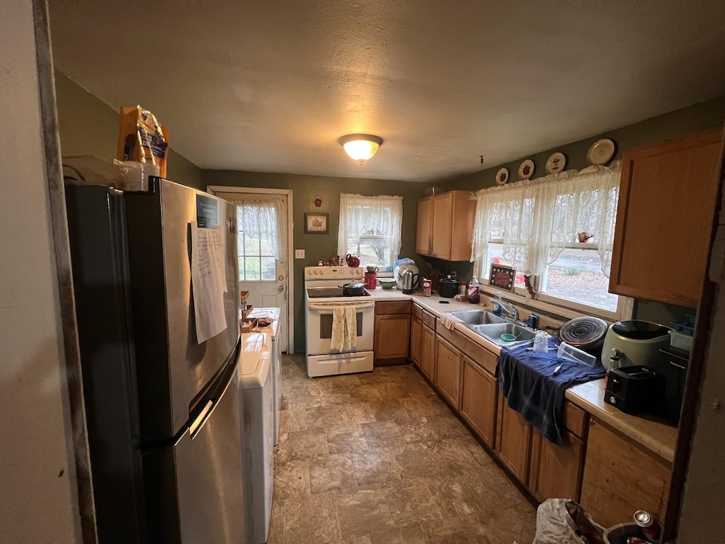 kitchen with white electric range oven, a textured ceiling, sink, washing machine and clothes dryer, and stainless steel refrigerator