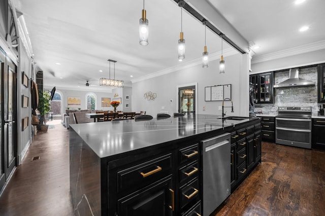 kitchen featuring sink, wall chimney exhaust hood, pendant lighting, a kitchen island with sink, and appliances with stainless steel finishes