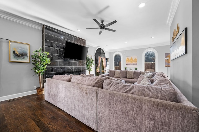 living room with ceiling fan, ornamental molding, dark wood-type flooring, and a tile fireplace