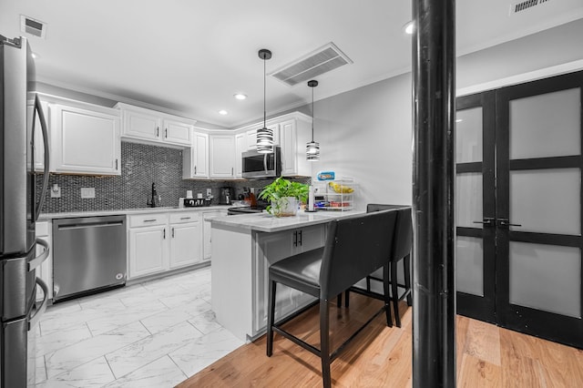 kitchen featuring stainless steel appliances, crown molding, pendant lighting, a breakfast bar area, and white cabinets