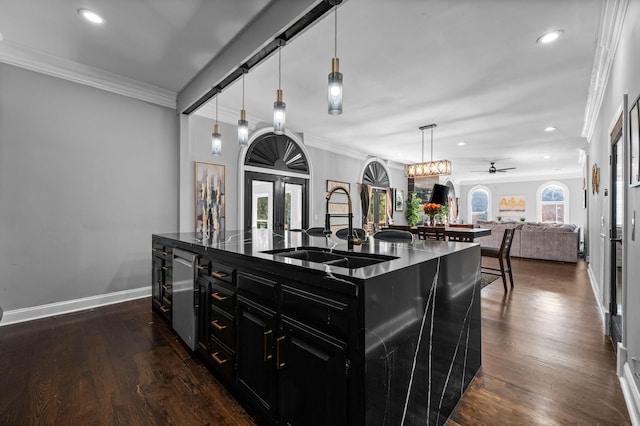 kitchen with ornamental molding, ceiling fan, a kitchen island with sink, sink, and pendant lighting