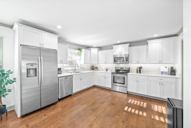 kitchen featuring white cabinetry, sink, light hardwood / wood-style floors, decorative backsplash, and appliances with stainless steel finishes