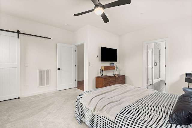 bedroom with a barn door, ceiling fan, carpet floors, and ensuite bathroom