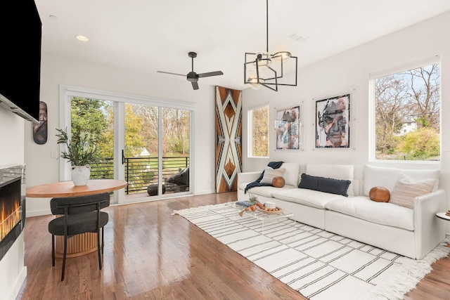 living room featuring ceiling fan with notable chandelier and light wood-type flooring