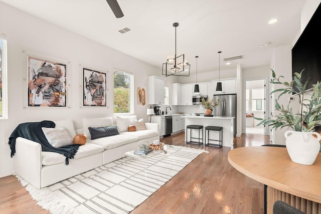 living room featuring ceiling fan with notable chandelier and light hardwood / wood-style floors