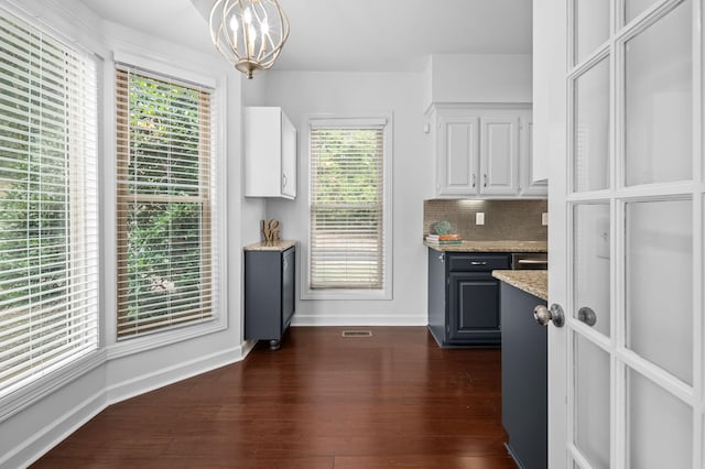 kitchen with light stone countertops, hanging light fixtures, a notable chandelier, backsplash, and white cabinets