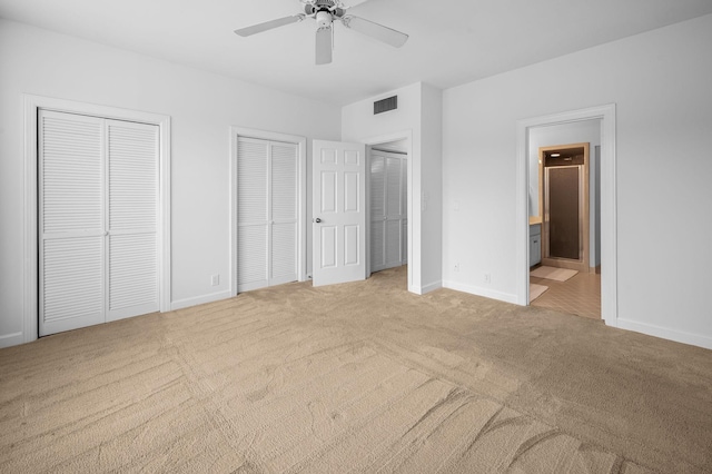 unfurnished bedroom with ensuite bathroom, ceiling fan, light colored carpet, and two closets