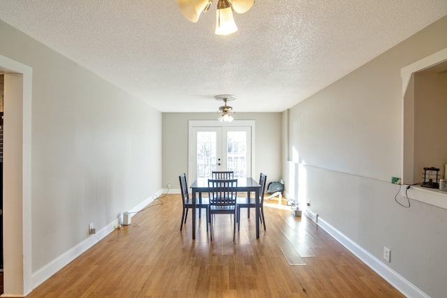 unfurnished dining area featuring ceiling fan, light wood-type flooring, a textured ceiling, and french doors