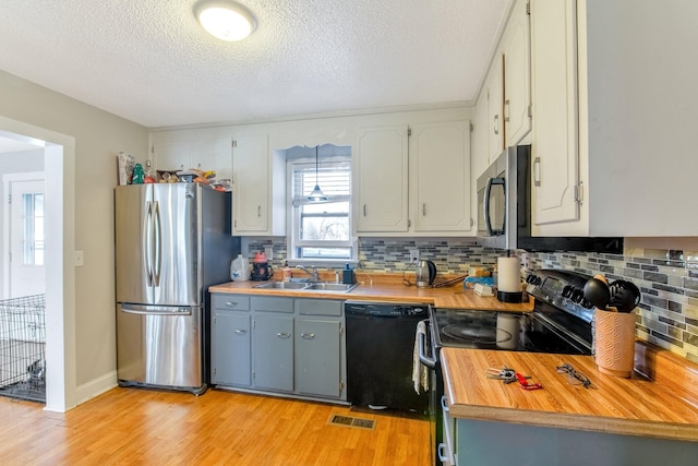 kitchen with black appliances, sink, light wood-type flooring, a textured ceiling, and tasteful backsplash