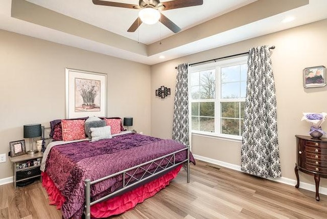 bedroom with hardwood / wood-style floors, a tray ceiling, and ceiling fan