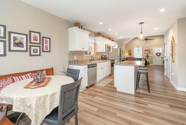 kitchen with pendant lighting, appliances with stainless steel finishes, white cabinetry, light stone countertops, and a kitchen island