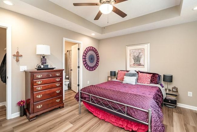 bedroom with connected bathroom, a raised ceiling, and light wood-type flooring